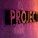 Betonwand im Fabverlauf Lila bis Orange angestrahlt. Auf der Wand ist das englische Wort "PROJECTS" notiert.