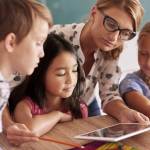 Lehrerin mit Kindern zeigt ihnen den Umgang mit einem Tablett.