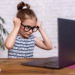 Junges Mädchen schaut mit übergroßer Brille auf einen Laptop-Bildschirm.