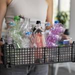 Ausschnitt zeigt eine Frau, die einen Korb voll leerer Plastikflaschen vor ihrem Bauch trägt.