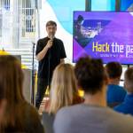Moderator spricht vor Publikum mit einer Präsentation zum Hackathon "Hack the paradise!"