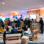 viele Menschen vor einem aus Holz gebauten Messestand, die sich unterhalten