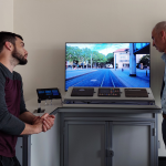 In der Mitte der neue Fahrerstand beim Nahverkehr zum Trainieren des Fahrassistenzsystem. Daneben stehen rechts und links 2 Männer, diese sehen sich auf dem Computer in der Mitte das neue System an.
