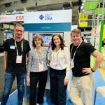 Vier Menschen lachen vor einem Messestand in die Kamera.