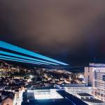 Die Gebäude in Jena erstrahlen im Dunkeln, am Himmel ist ein großer Laserstrahl.