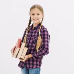 Mädchen mit Zöpfen und Büchern in der Hand lacht in die Kamera.