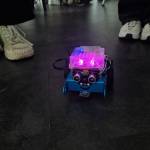 In der Mitte des Raums steht ein lila-leuchtender kleiner Roboter.