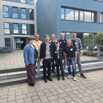 Gruppe von Menschen steht vor einer Schule und lächelt in die Kamera.