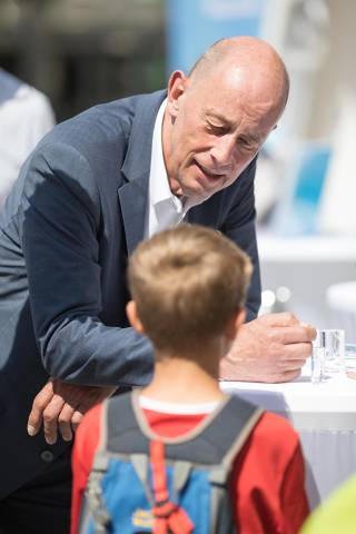 Minister Wolfgang Tiefensee spricht auf einen Stehtisch gelehnt mit einem Kin, dass einen Rucksack auf dem Rücken trägt.