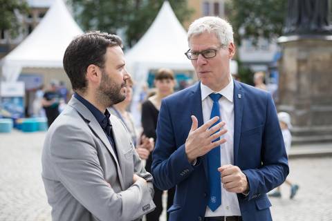 Von links Dezernent Benjamin Koppe im Gespräch mit Dr. Thomas Knoll (Referat für Digitales und Kreativwirtschaft - TMWWDG). Im Hintergrund ein unscharfer Blick über den Marktplatz.