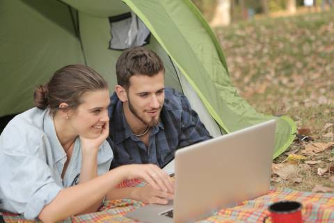 Ein Mann und eine Frau liegen in einem Zelt und schauen gemeinsam auf einen Laptop.