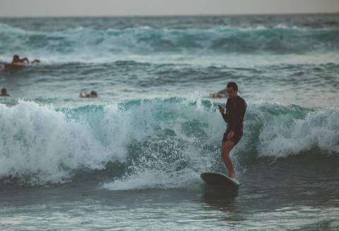 Mann surft auf einer Welle mit Smartphone in der Hand.