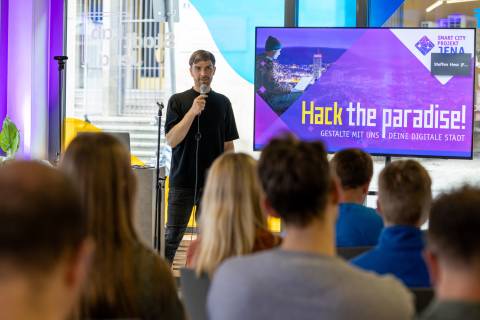 Moderator spricht vor Publikum mit einer Präsentation zum Hackathon "Hack the paradise!"
