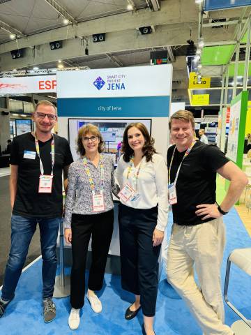 Vier Menschen lachen vor einem internationalen Messestand in die Kamera.