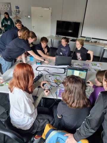 Viele Kinder sind in einem Raum mit Technik und schauen auf einen Monitor.