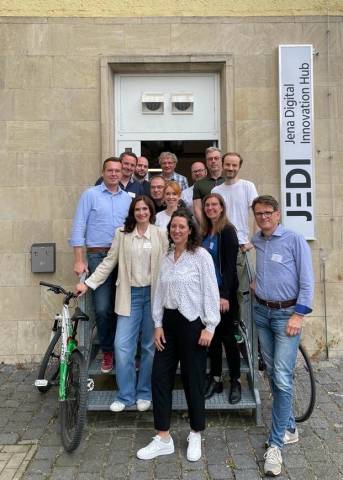 Teilnehmende stehen aufgereiht, auf und neben einer Treppe, vor einem Eingang, auf einem Schild steht: JEDI - Jena Digital Innovation Hub