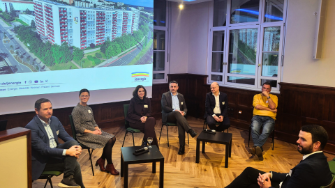Mehrere Menschen sitzen vorne auf Stühlen in einem Podium.