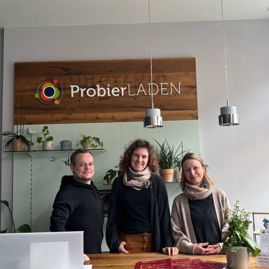 Das Team vom ProbierLaden steht am Empfangstresen und lächelt in die Kamera.