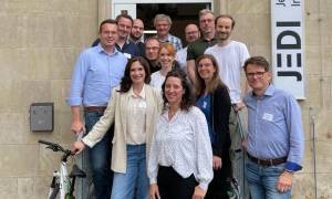 Teilnehmende stehen aufgereiht, auf und neben einer Treppe, vor einem Eingang, auf einem Schild steht: JEDI - Jena Digital Innovation Hub