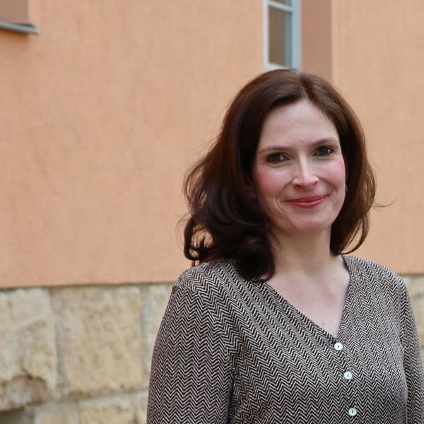 Eine Frau steht lächelnd vor einer orangenen Hauswand