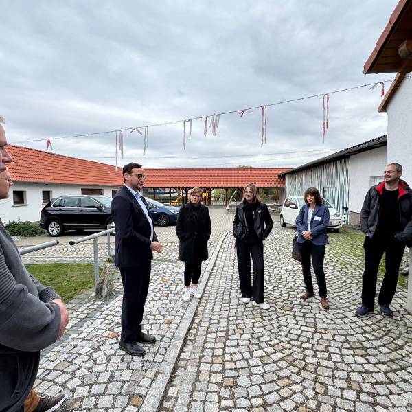 Mehrere Menschen stehen im Halbkreis und hören einem Mann zu.