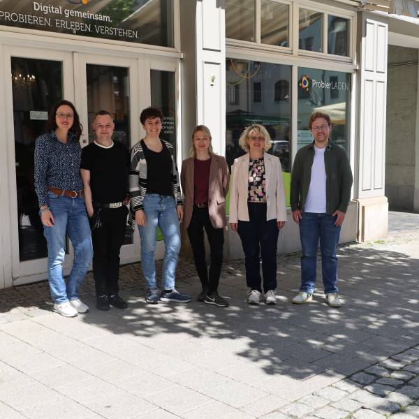 6 Personen ( v.l. Nicole Bergmann, Oliver Ephrosi Menchau, Anna Geißler, Sara Delinger-Parcetic, Dr. Angela Anding, Lokas Dorn) stehen vor einem Laden mit der Aufschrift "ProbierLaden - Digital gemeinsam. Probieren. Erleben. Verstehen." 