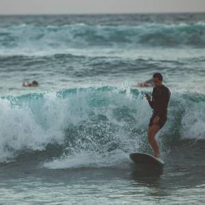 Mann surft auf einer Welle mit Smartphone in der Hand.