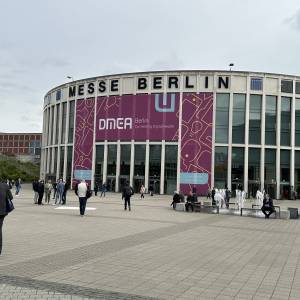 Das Messegelände in Berlin von außen mit einem großen Plakat "DMEA Berlin Connecting Digital Health", ringsherum sieht man Menschen durch die Gegend laufen.