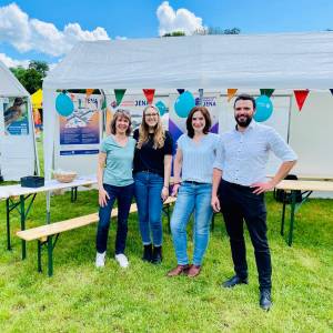 v.l.: Heike Stötzner, Vanessa Huber, Dorothea Prell und Dezernent Benjamin Koppe stehen vor dem Smart City Stand bei "Dein Tag im Paradies" 2024. . Im Hintergrund sieht man ein Zelt mit Plakaten des Projekts "5G-Verkehrsvernetznung" und "Smart City Projekt".