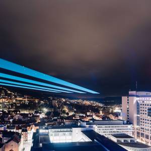 Die Gebäude in Jena erstrahlen im Dunkeln, am Himmel ist ein großer Laserstrahl.