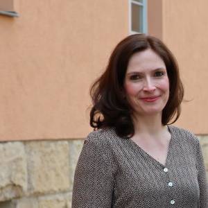 Eine Frau steht lächelnd vor einer orangenen Hauswand