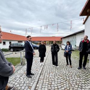 Mehrere Menschen stehen im Halbkreis und hören einem Mann zu.
