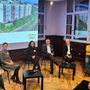 Mehrere Menschen sitzen vorne auf Stühlen in einem Podium.