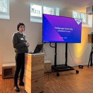 Olivia Busch stehtam Rednerpult mit Bildschirm.