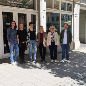 6 Personen ( v.l. Nicole Bergmann, Oliver Ephrosi Menchau, Anna Geißler, Sara Delinger-Parcetic, Dr. Angela Anding, Lokas Dorn) stehen vor einem Laden mit der Aufschrift "ProbierLaden - Digital gemeinsam. Probieren. Erleben. Verstehen." 