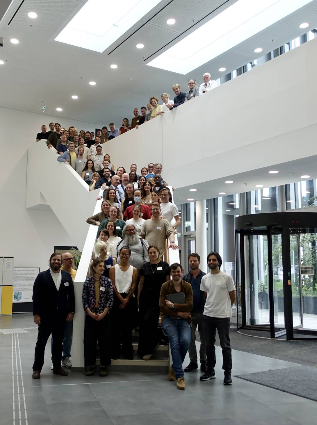 Gruppe von vielen Menschen stehen auf einer Treppe und lächeln in die Kamera.