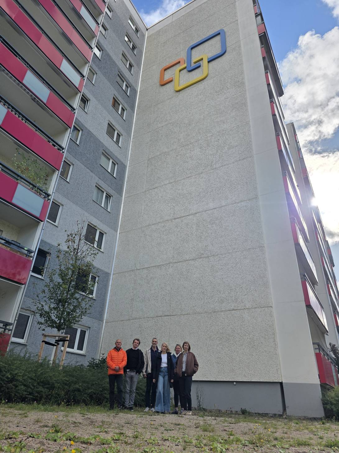 Mehrere Menschen stehen vor einem Hochhaus und schauen in die Kamera.